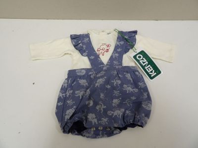 une combinaison pour bébé, avec une chemise blanche et une salopette bleue, posée sur une table