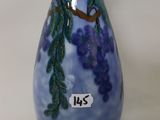 a blue vase with purple grapes on it on a white surface