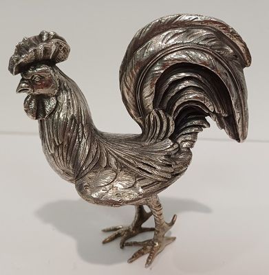 une figurine de coq en argent posée sur un fond blanc