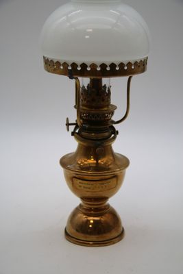 une lampe ancienne en laiton, surmontée d'un abat-jour en verre blanc