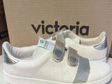 des baskets blanches et argentées, ornées de lanières argentées, exposées devant une boîte