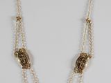 un collier en or composé d'une longue chaîne et de deux perles pendantes