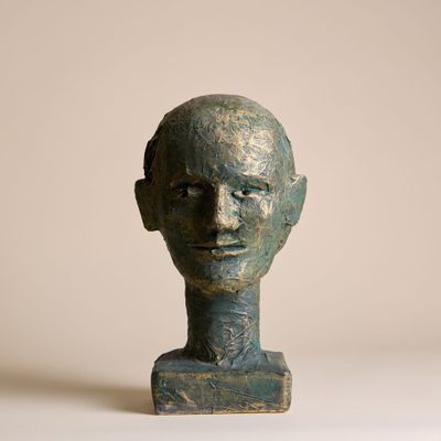 sculpture représentant une tête d'homme posée sur un socle, sur fond beige