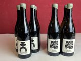 Trois bouteilles de vin sont posées sur une table, avec un mur rouge en arrière-plan.