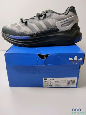 une paire de chaussures Adidas posée sur une boîte bleue