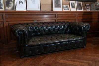 un canapé en cuir noir dans une pièce où sont accrochés des tableaux aux murs