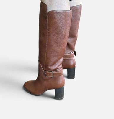 une paire de bottes marron pour femme, portées avec des chaussettes blanches et un legging noir