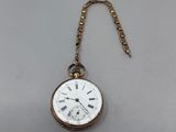 une montre de poche ancienne à laquelle est accrochée une chaîne sur le côté
