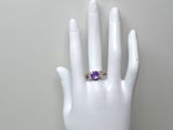 une image représentant la main d'une femme tenant une bague sertie d'une pierre violette