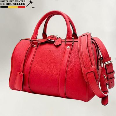 the red handbag is sitting on a white surface with a black handle