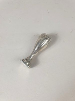 un vase ancien en argent posé sur une surface blanche, avec un petit morceau de métal
