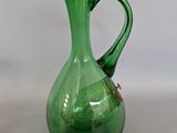 un pichet en verre vert muni d'une anse, posé sur une surface blanche