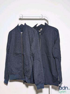 two jackets hanging on a clothes rack against a white wall