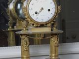 a gold clock sitting on a marble pedestal in front of a window