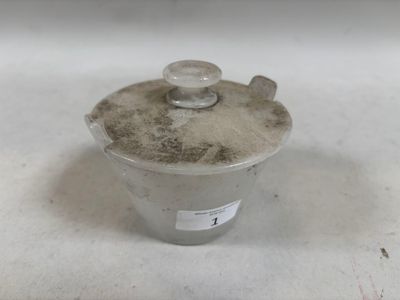 un petit récipient en métal muni d'un couvercle, posé sur une surface blanche
