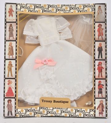 poupée vêtue d'une robe blanche avec un nœud rose, dans une boîte