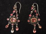 une paire de boucles d'oreilles roses et argentées posées sur un fond noir