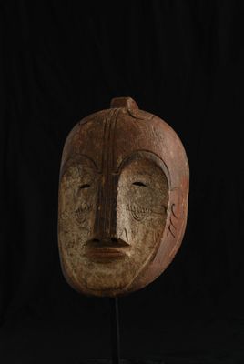 un gros plan d'un masque en bois posé sur un socle, sur fond noir