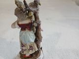 une figurine représentant une femme tenant un oiseau perché sur une branche