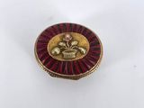 a close up of a red and gold broocher on a white surface