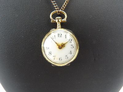 une petite montre de poche en or suspendue à un collier sur un mannequin