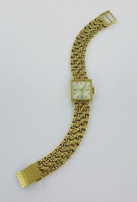 une montre-bracelet en or avec un cadran blanc posée sur un fond blanc