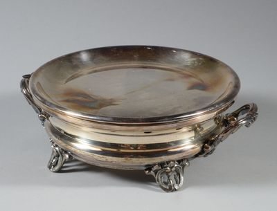 un plat ancien en argent avec des poignées, posé sur un socle, sur fond blanc