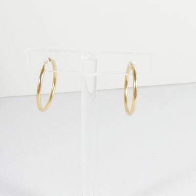 une paire de boucles d'oreilles créoles en or posée sur un présentoir transparent