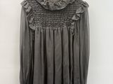 grey blouse with ruffles on a hanger against a white wall