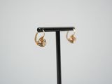 a pair of gold earrings on a black stand