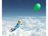 un petit garçon qui vole dans le ciel avec un ballon vert