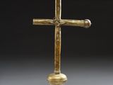 a gold cross on a black stand with a white background