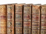 several old books are lined up in a row on a white surface