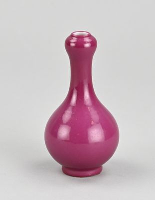 un vase violet posé sur une surface blanche, sur fond gris
