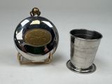 une tasse en argent posée à côté d'une flasque en argent sur une table