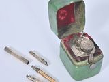 a green box with a silver object inside and a pen in it