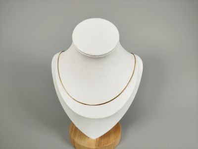 collier blanc et doré posé sur un support en bois, sur fond gris