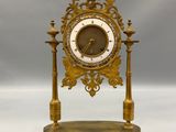 une horloge dorée posée sur un socle, sur fond blanc