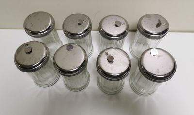 six bocaux en verre munis de couvercles argentés sont alignés sur une surface blanche