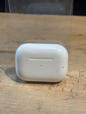 Des AirPods de la marque Apple sont posés sur une table en bois, dans un étui transparent