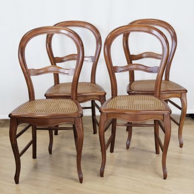 four wooden chairs with wicker seats in a row against a white wall