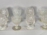 six glass goblets and cups are lined up on a white surface