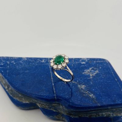 une bague sertie d'une émeraude et de diamants, posée sur une pierre bleue