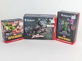 Trois boîtes de cartes « Magic : The Gathering » sont posées sur une surface blanche.