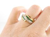 a woman ' s hand holding a ring with a diamond and emerald band