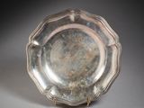un plat ancien en argent posé sur un socle, sur une surface grise