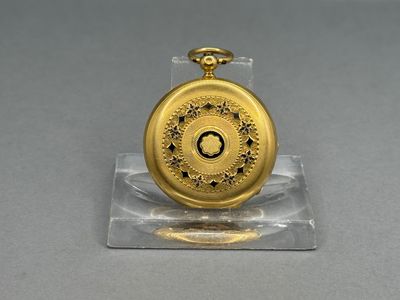 a gold pocket watch on a clear stand on a table