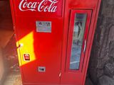 a red coca cola machine sitting on the side of a building