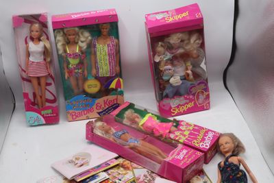 Plusieurs poupées Barbie sont posées sur une surface blanche, à côté d'une boîte remplie de livres