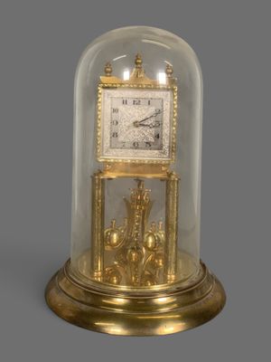 une image représentant une horloge en or posée sur une table, sous un dôme en verre